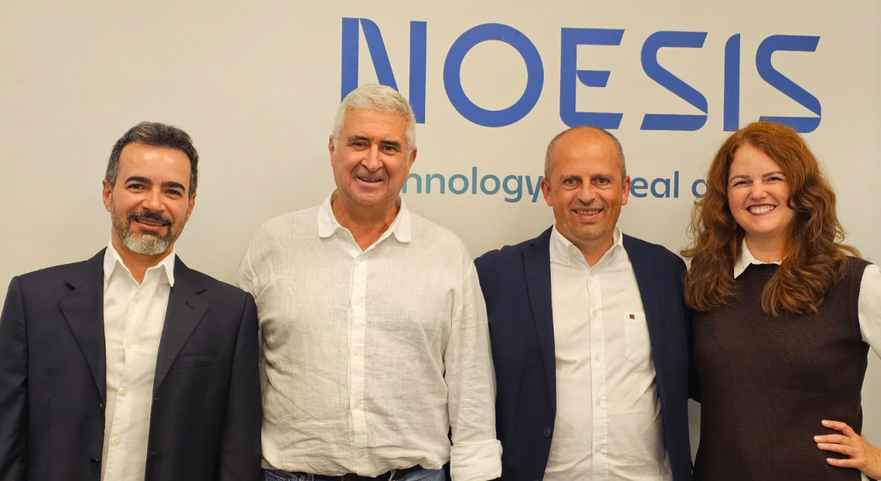Quatro pessoas posam juntas em frente a um painel da Noesis, incluindo o CEO Alexandre Rosa, de camisa branca